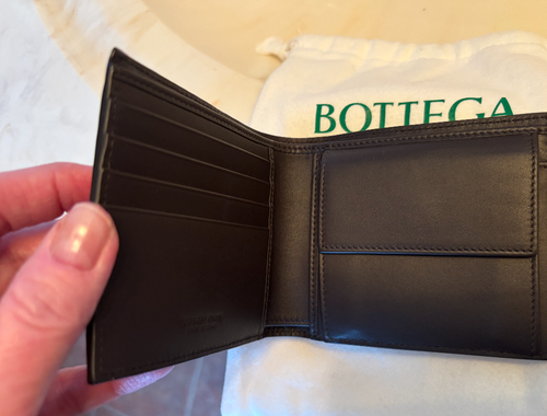 Black leather wallet held open with a Bottega Veneta branded background